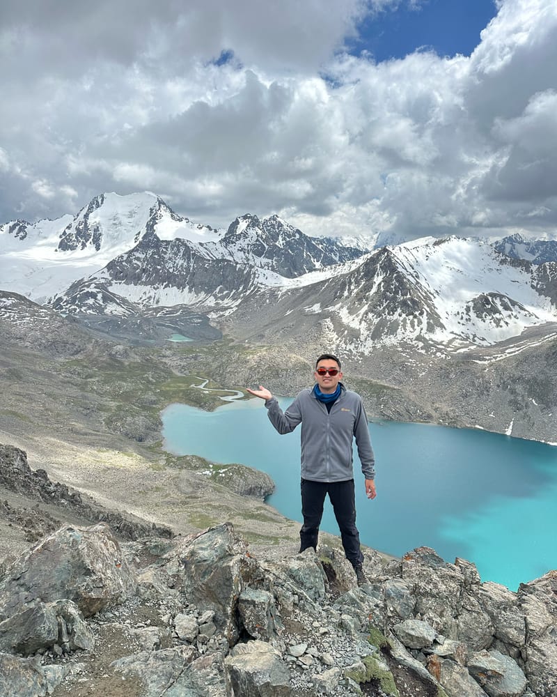 Průvodce Beka ukazuje na tyrkysové jezero Ala-Kul pod zasněženými štíty